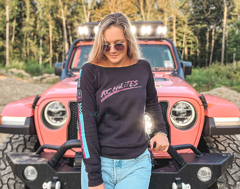 KC HiLiTES Ambassador @alexinthepeachjeep in a new KC black long sleeve with her Jeep Wrangler JL behind.